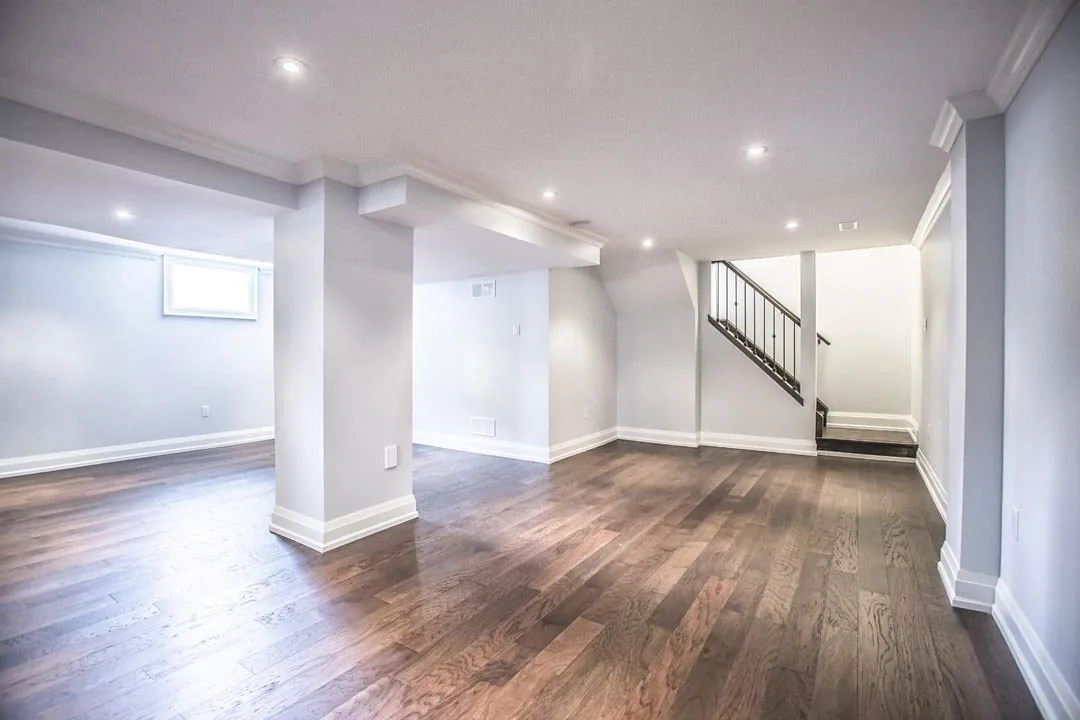 Finished basement with hardwood flooring, white trim, and a staircase