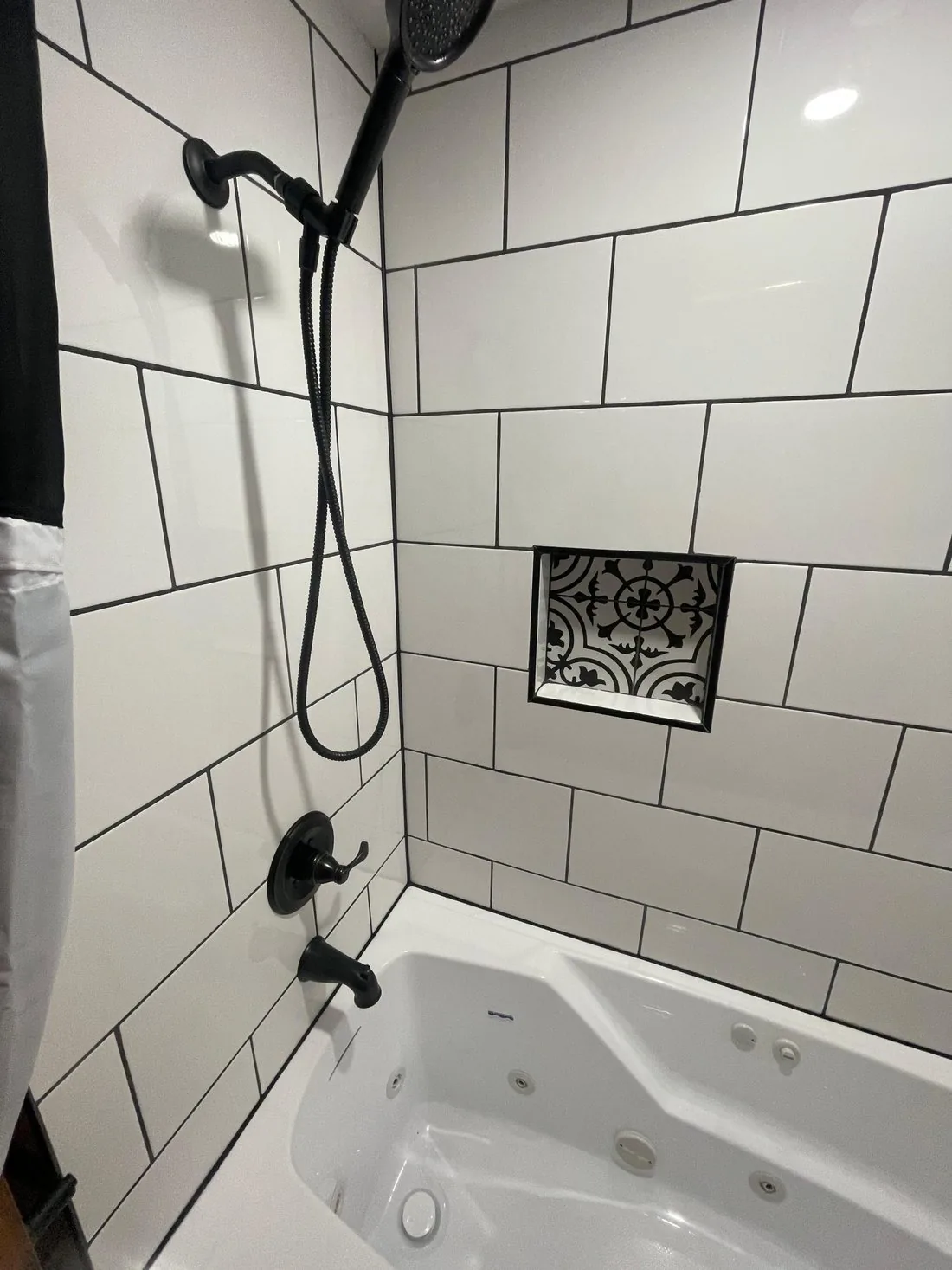Tiled tub and shower with black fixtures and a patterned tile niche