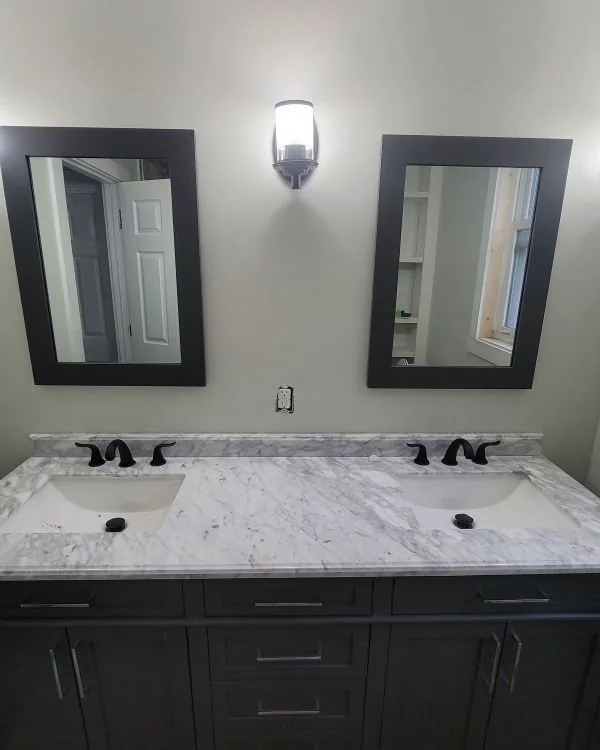 Double vanity with a marble top, dark cabinetry, and framed mirrors