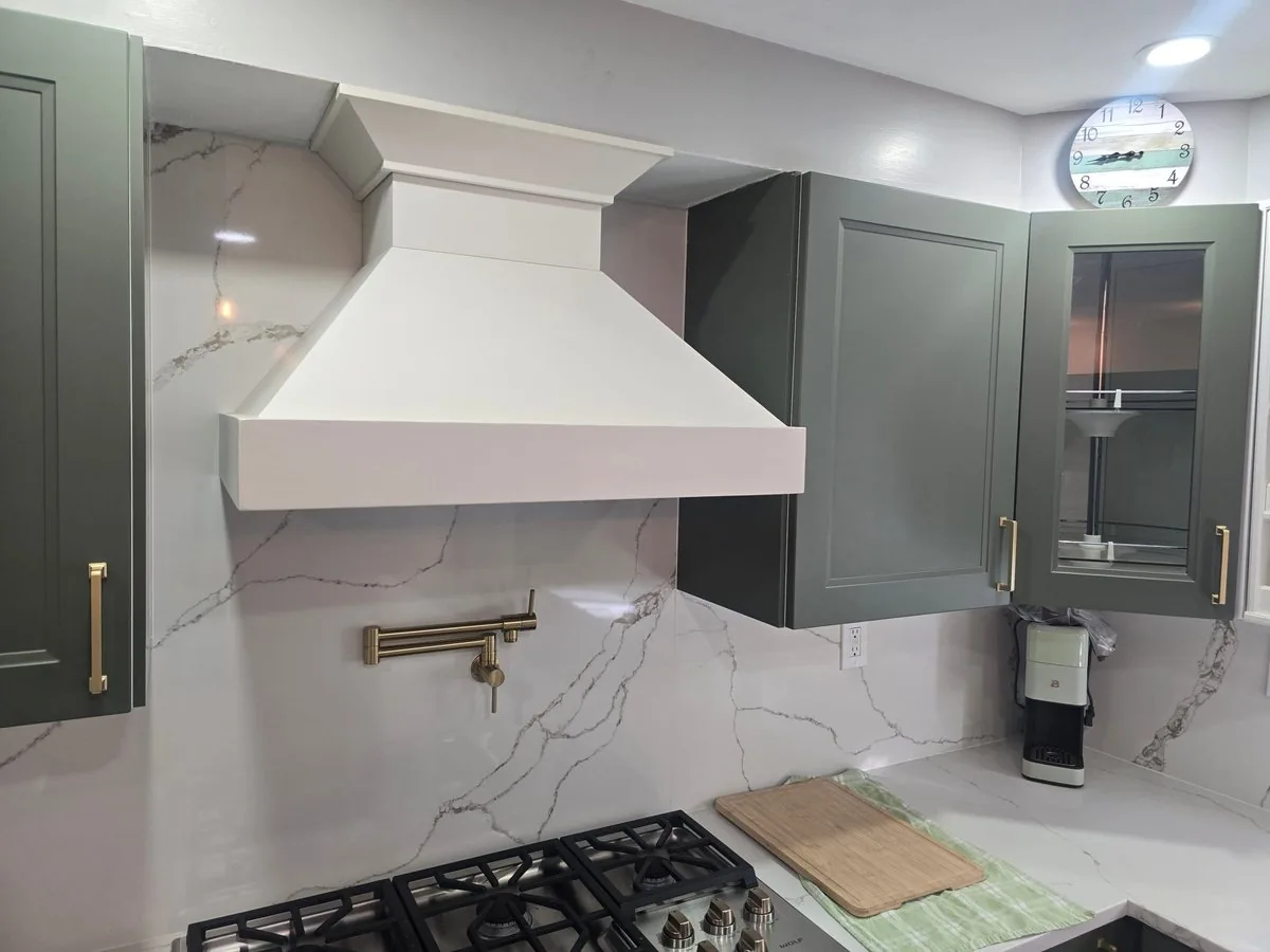 Plaster range hood over a gas range with a marble backsplash and green cabinetry
