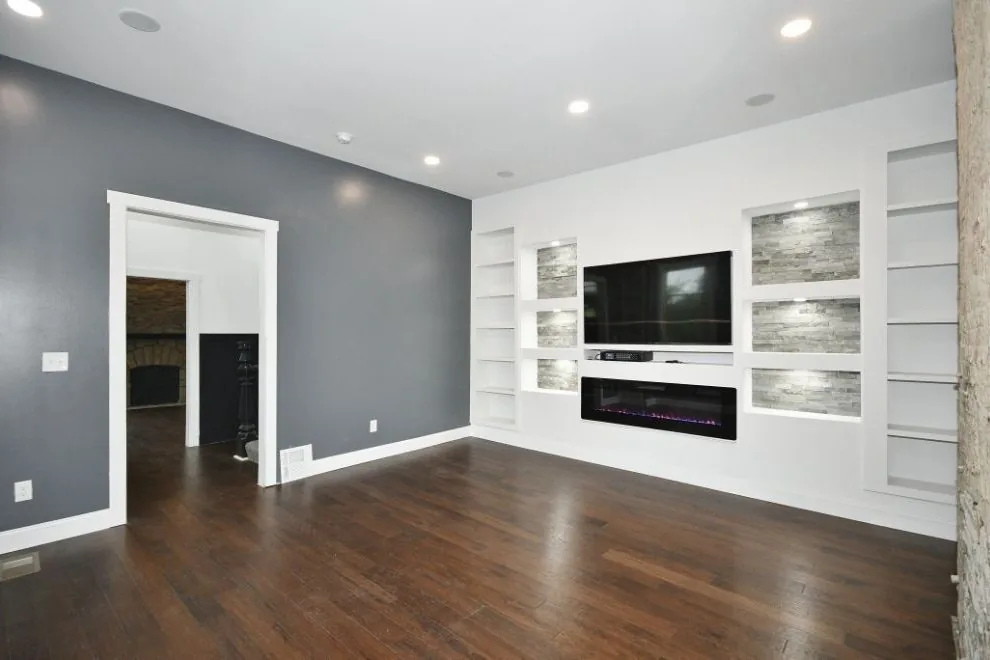 Living room with white built-in shelving, a linear fireplace, and dark hardwood floors