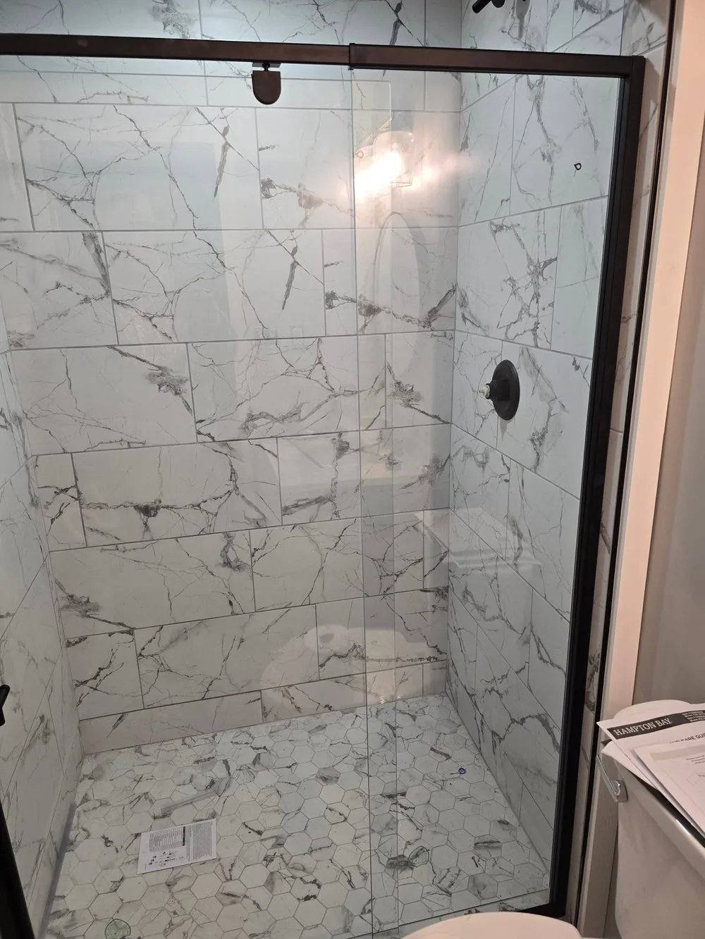 Walk-in shower finished in large-format marble-look tile with a glass door